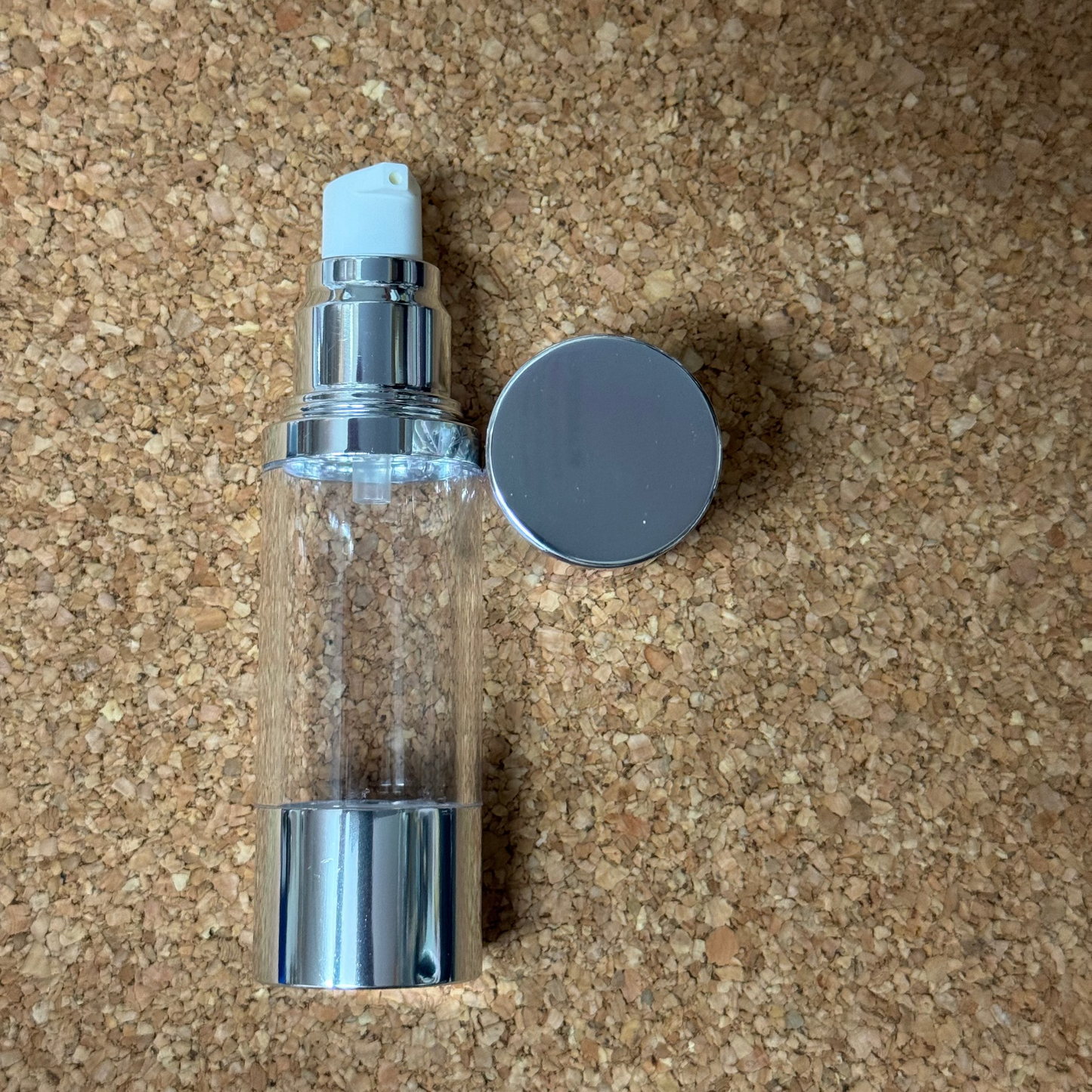 Clear spray bottle with silver nozzle and cap on a cork background