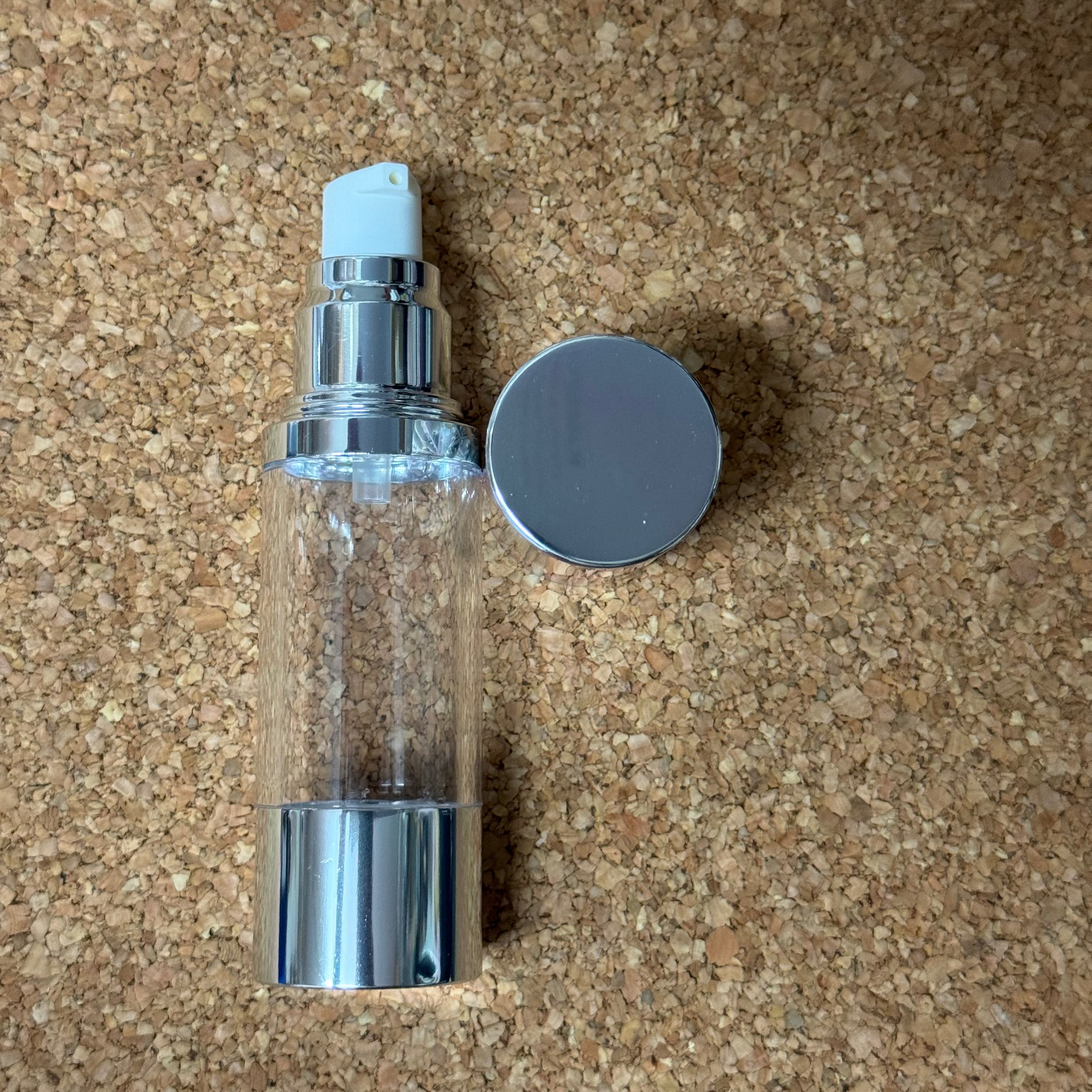 Clear spray bottle with silver nozzle and cap on a cork background