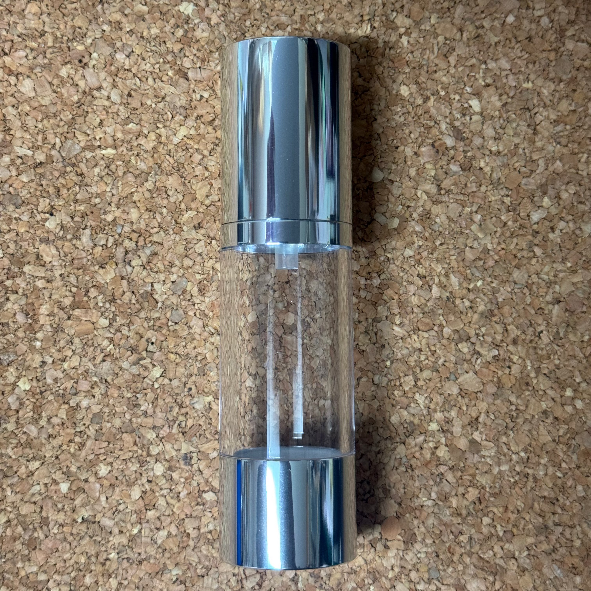 Clear cylindrical bottle with silver cap on a cork background